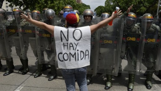 A woman with a sign reading "There is no food" protests in front of a line of policemen in Caracas